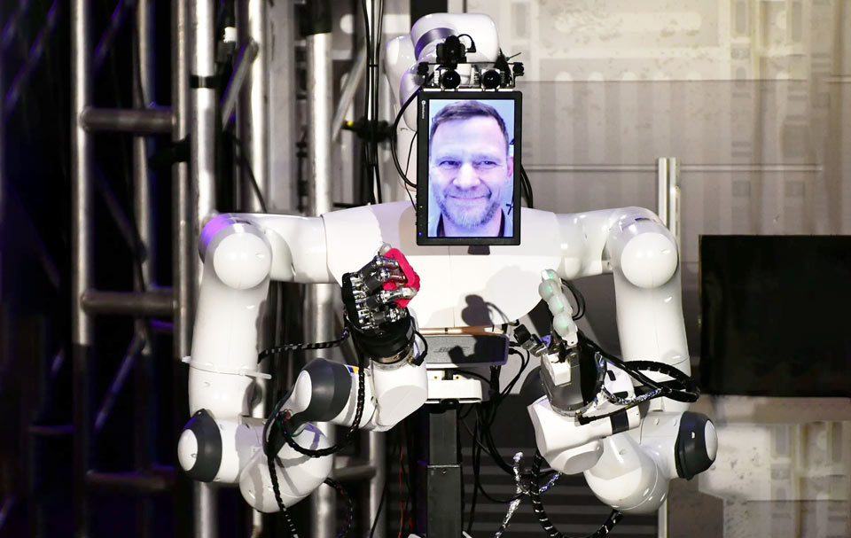 Робот тримає червоний камінь, а на екрані зображений усміхнений бородатий чоловік.